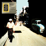 Album cover art for Buena Vista Social Club's 20th Anniversary World Tour, featuring a man walking down a sunlit street with vintage cars on the right, with a vinyl record sleeve graphic overlaid in the top-left corner.