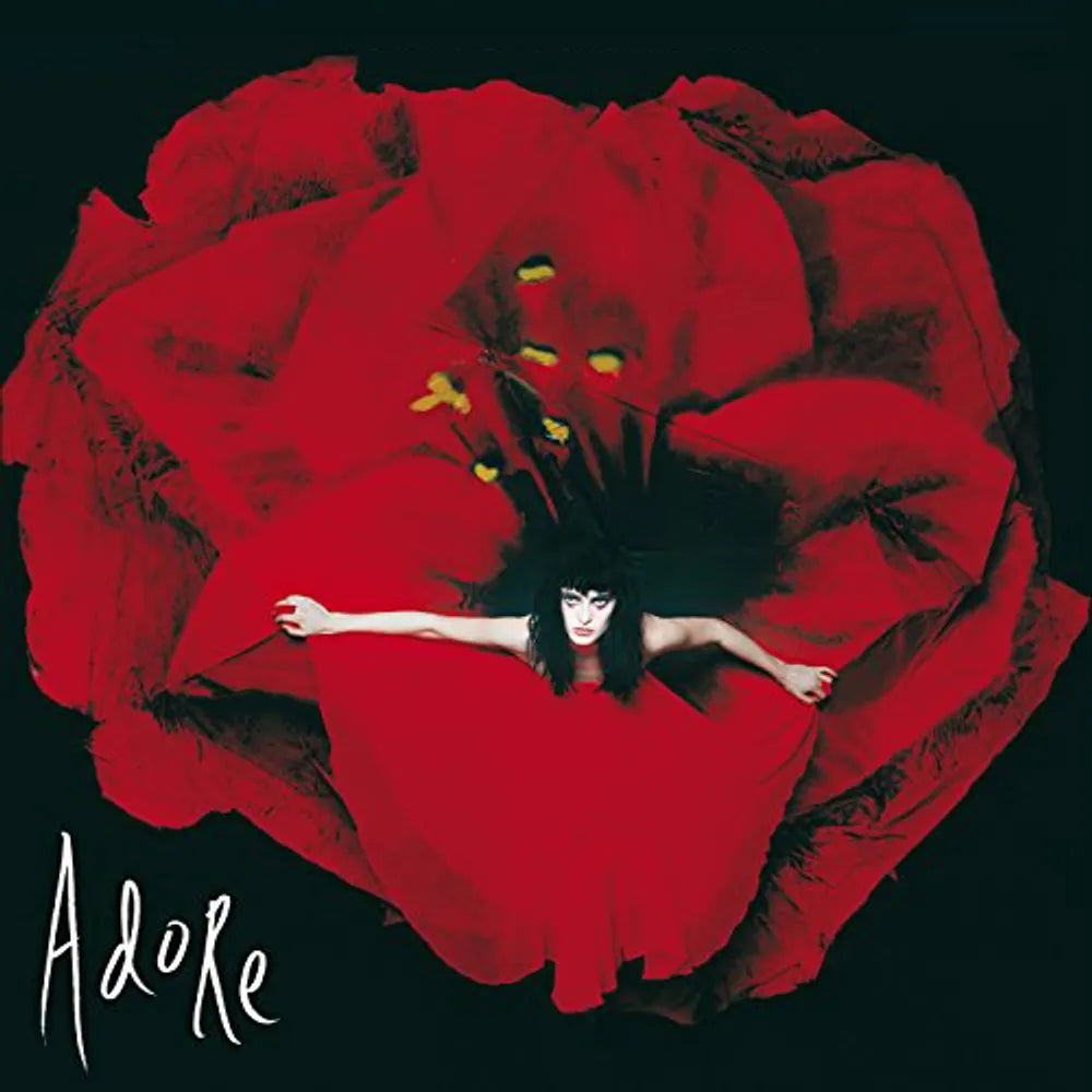 Album cover art for 'Adore' featuring a woman in a red dress spread out like petals on a large red flower against a black background, with the word 'Adore' in white script at the bottom left.