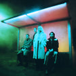 Four people sitting inside a colorful, abstract light box.