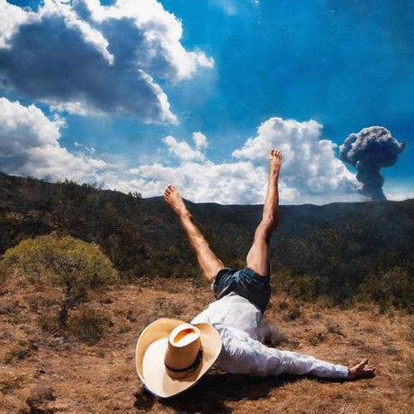 Person lying on their back with legs in the air, wearing a hat, with a volcanic eruption in the background.