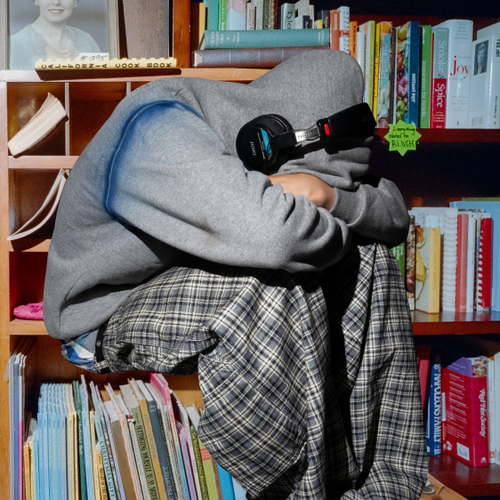 Person wearing headphones and a hoodie sitting among bookshelves