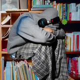 Person wearing headphones and a hoodie sitting among bookshelves