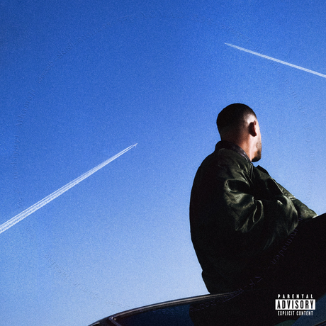 Person sitting on a car with a clear blue sky and contrails in the background