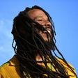 Person with dreadlocks wearing a yellow shirt against a blue sky
