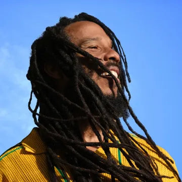 Person with dreadlocks wearing a yellow shirt against a blue sky