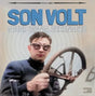 Album cover for 'Sound Signal Serenades' by Son Volt featuring a person with goggles holding a steering wheel.