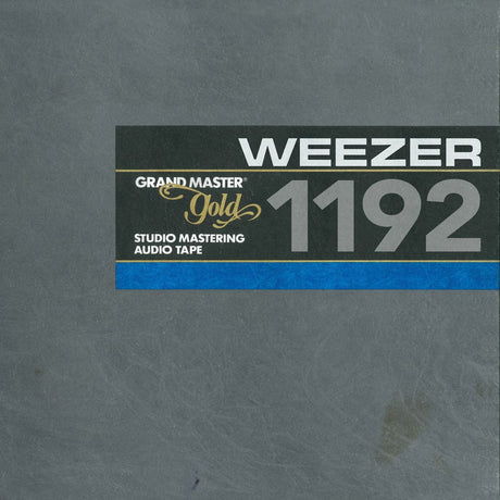 The front cover of a Weezer Grand Master Gold 1192 Studio Mastering Audio Tape, featuring a textured gray background with a black label containing white and gold text and a blue stripe.
