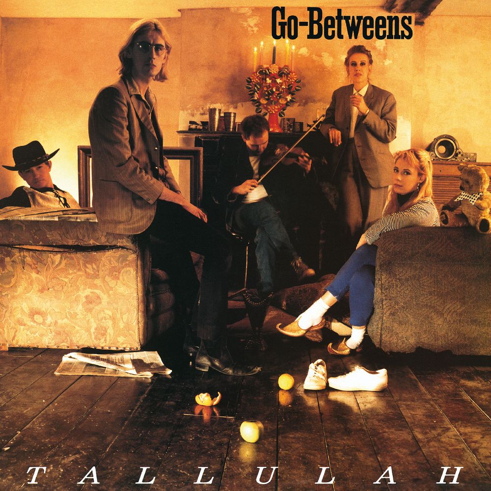 Album cover for Tallulah's 'Go-Betweens', featuring five band members posed in a warmly lit, rustic room with the title 'Go-Betweens' at the top and 'TALLULAH' at the bottom.