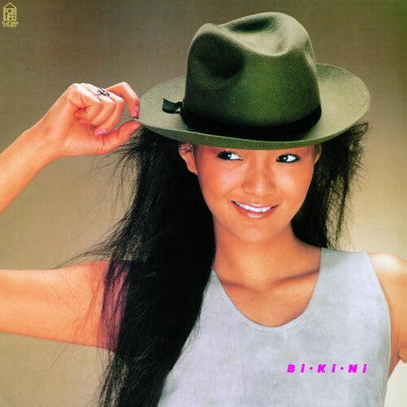 Anri wearing a green hat, smiling, with long black hair. She is holding a cigarette in her hand, and the background is a solid color.