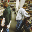 Two people browsing through records in a store, with a variety of vinyl records visible in the background.