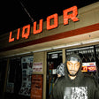 A person standing in front of a liquor store at night, wearing a hoodie with a graphic design.