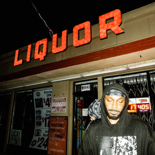 A person standing in front of a liquor store at night, wearing a hoodie with a graphic design.