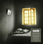 The image depicts the cover of the album 'Dog Man Star' by the band Suede, celebrating its 30th anniversary. The cover features a black and white photograph of a person lying on a bed in a dark room, with a yellow window frame illuminating the space.