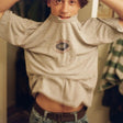 Person wearing a beige sweatshirt with a logo, standing indoors.