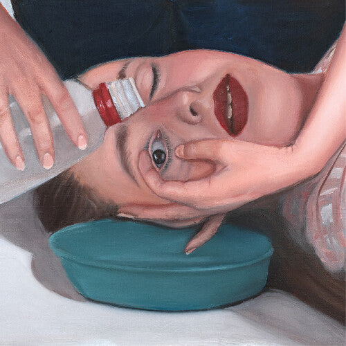 Person lying on a white surface with a teal bowl under their head, holding a bottle above their face.
