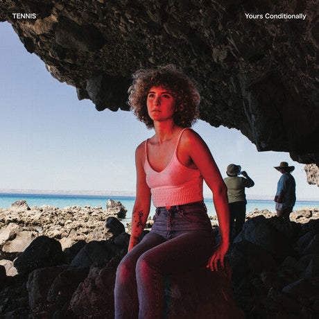 Person sitting on rocks by the ocean with 'Tennis' album cover in the background