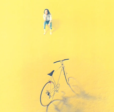 Person sitting on a bicycle against a yellow background