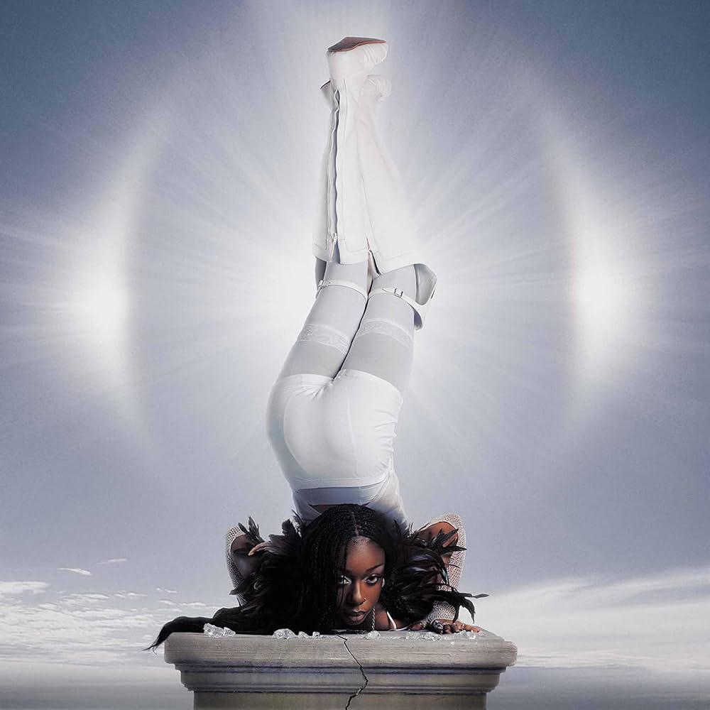 Person in a white outfit performing a handstand on a pedestal against a light gray background