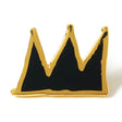 A small crown-shaped enamel pin with a gold metal outline and black enamel fill, photographed on a plain white background.