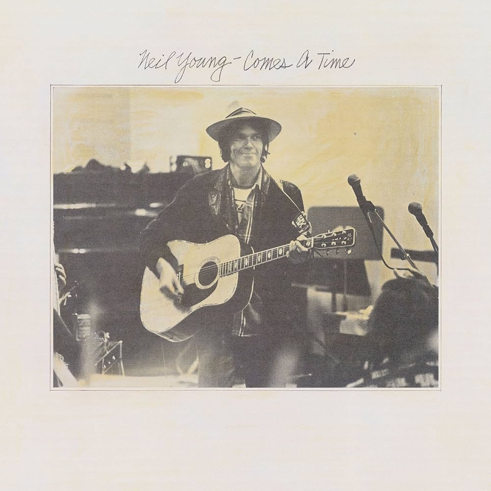 Album cover with a person holding a guitar, featuring text 'Neil Young - Comes A Time'.