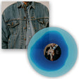 Blue vinyl record with a person's face on it, next to a denim jacket.