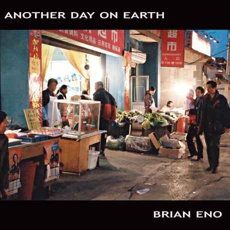 Album cover for Brian Eno's 'Another Day on Earth' featuring a photograph of a bustling Chinese street market at dusk, framed by black borders with white text.