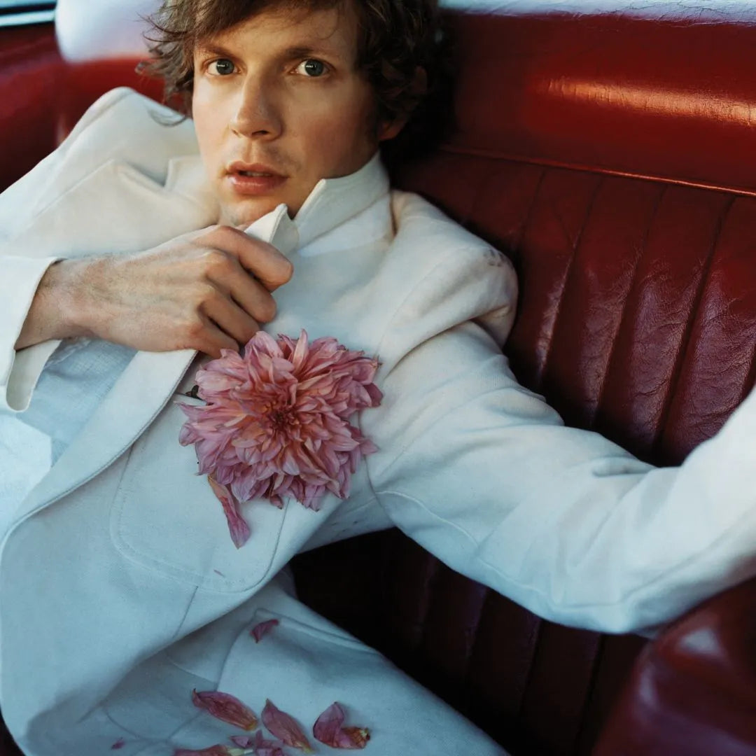 Person wearing a white outfit with a pink flower, sitting on a red leather couch.