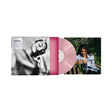 A vinyl record partially pulled from its album sleeve, shown on a white background. The record is pink, and the sleeve features a black-and-white portrait on the left and a color photograph of a woman sitting outdoors on the right.
