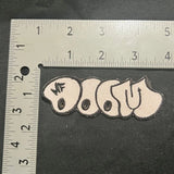 Embroidered patch with text on a black background, measured against a ruler.
