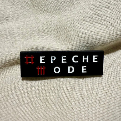 Black rectangular badge with 'EPECHE MODE' text on a beige fabric background