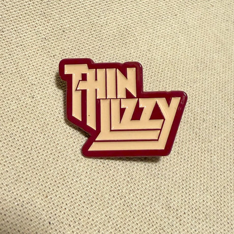 Thin Lizzy logo enamel pin on a beige fabric background