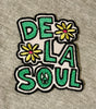 Embroidered patch with 'DE LA SOUL' text and flowers on a gray fabric background