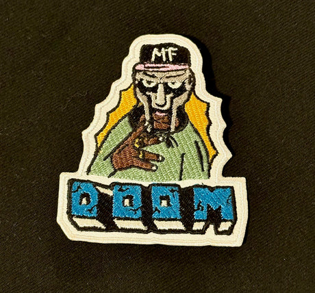 Embroidered patch with a character wearing a cap and holding a gun, with 'DOOM' text below on a black background.