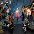 Group of people in a room with a blue curtain, one person in a pink dress, and a dog.