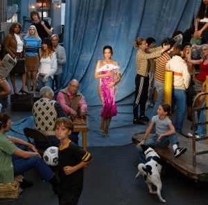 Group of people in a room with a blue curtain, one person in a pink dress, and a dog.