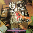 Album cover with a person holding a knife, surrounded by images of faces and tools on a table.