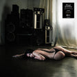 Person lying on the floor with tattooed body in a room with vintage speakers and a poster.