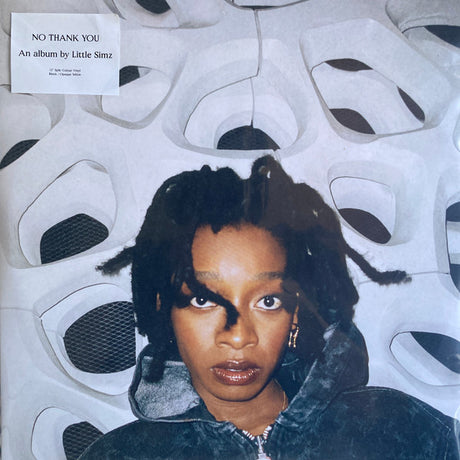 This image features the album cover of "No Thank You" by Little Simz, presented on a 2LP clear vinyl record. The album cover displays a striking portrait of Little Simz, capturing her intense gaze and distinctive style, set against a backdrop adorned with stylized, mask-like designs in white and grey tones.
