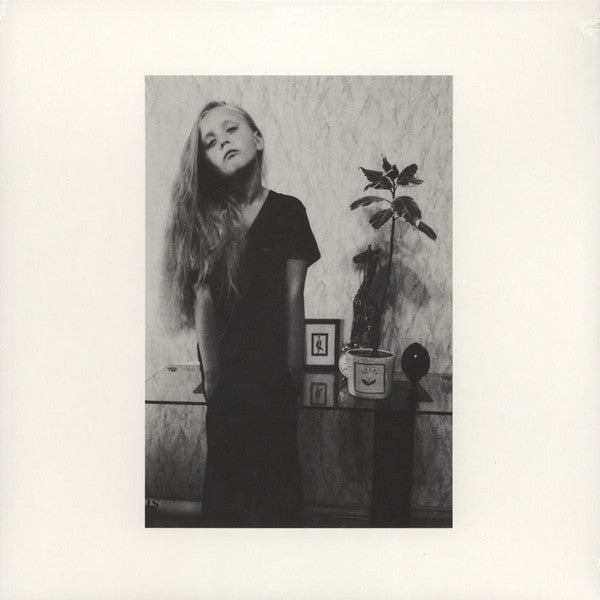 Black and white portrait of a woman in a room with a plant and framed picture.