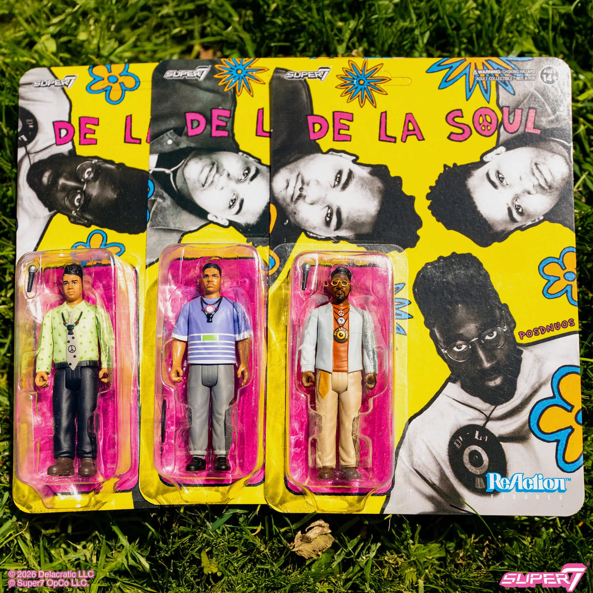 Packaged figures of De La Soul members with colorful packaging on grass