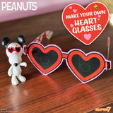 Heart-shaped glasses with a Snoopy figure and promotional text on a wooden surface.