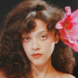 Woman with curly hair and a pink flower in her hair against a dark background