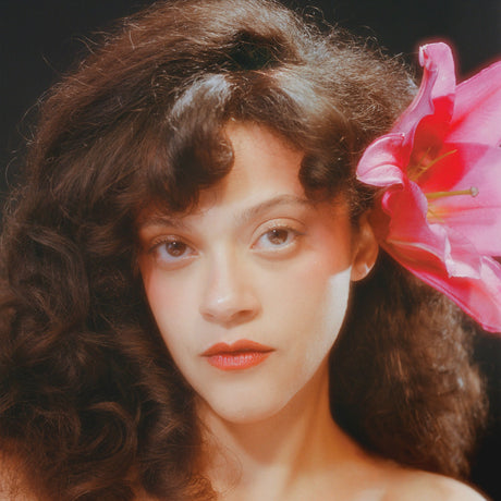 Woman with curly hair and a pink flower in her hair against a dark background