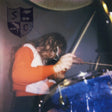 Person playing drums with a blue drum set in a dimly lit room.