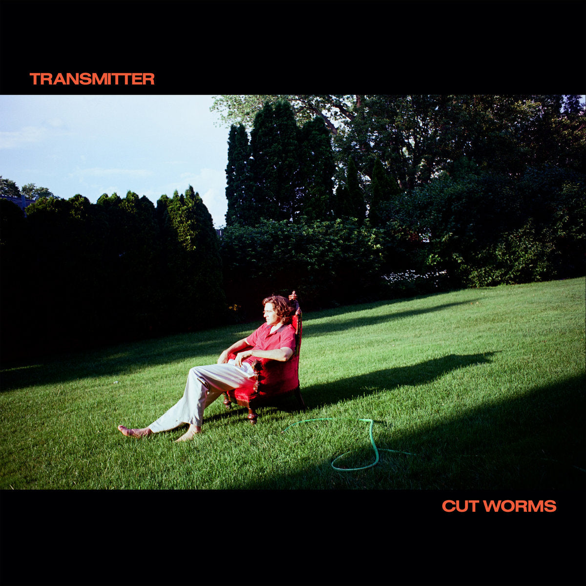 Person sitting in a red chair on grass with trees in the background, album cover for 'Transmitter' by Cut Worms.