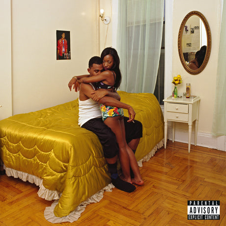 Two people embracing on a yellow bed in a room with a mirror and small table.