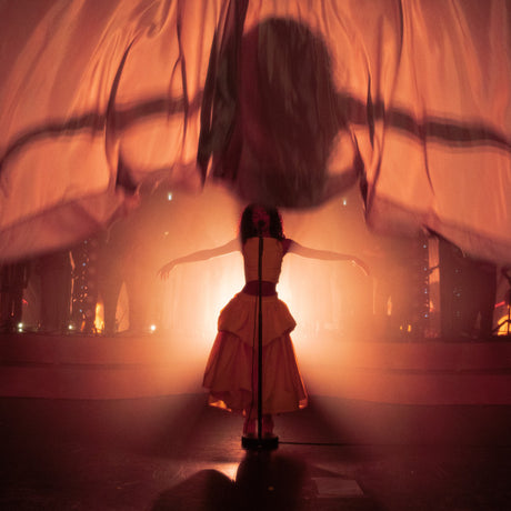 Person in a white dress standing on a stage with a warm, orange glow