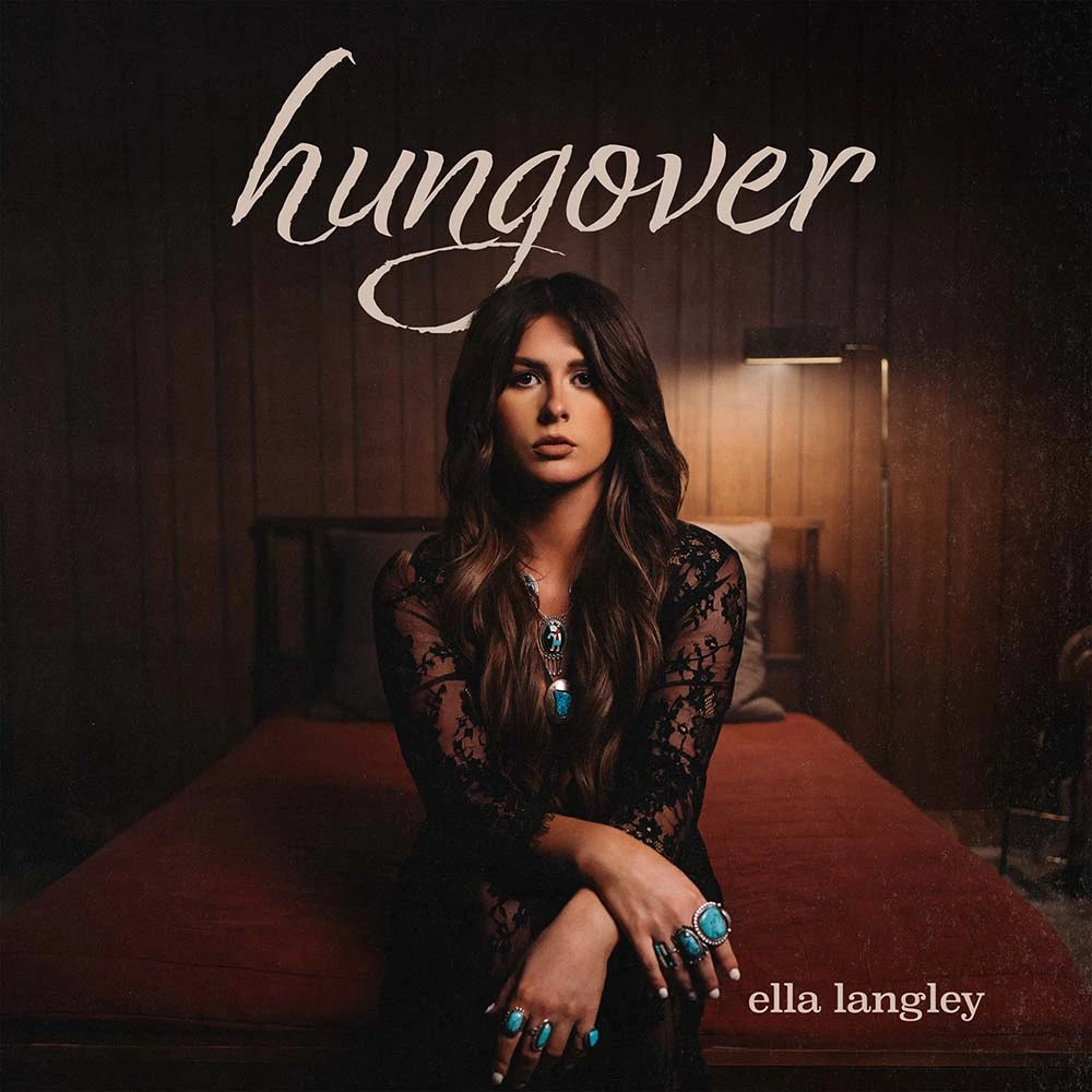 Album cover for Ella Langley's 'Hungover', featuring the artist sitting on a bed in a dimly lit room with wood-paneled walls, wearing a black lace top and turquoise jewelry.
