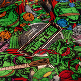 Close-up of a printed fabric featuring the Teenage Mutant Ninja Turtles character art and logo patch design, with green turtles, red and blue masks, and black background.