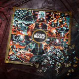 A Star Wars themed jigsaw puzzle box and loose pieces displayed on a dark, textured surface. The box features a detailed collage of iconic Star Wars characters and scenes, with the Star Wars logo centered in a gold-bordered circular frame.